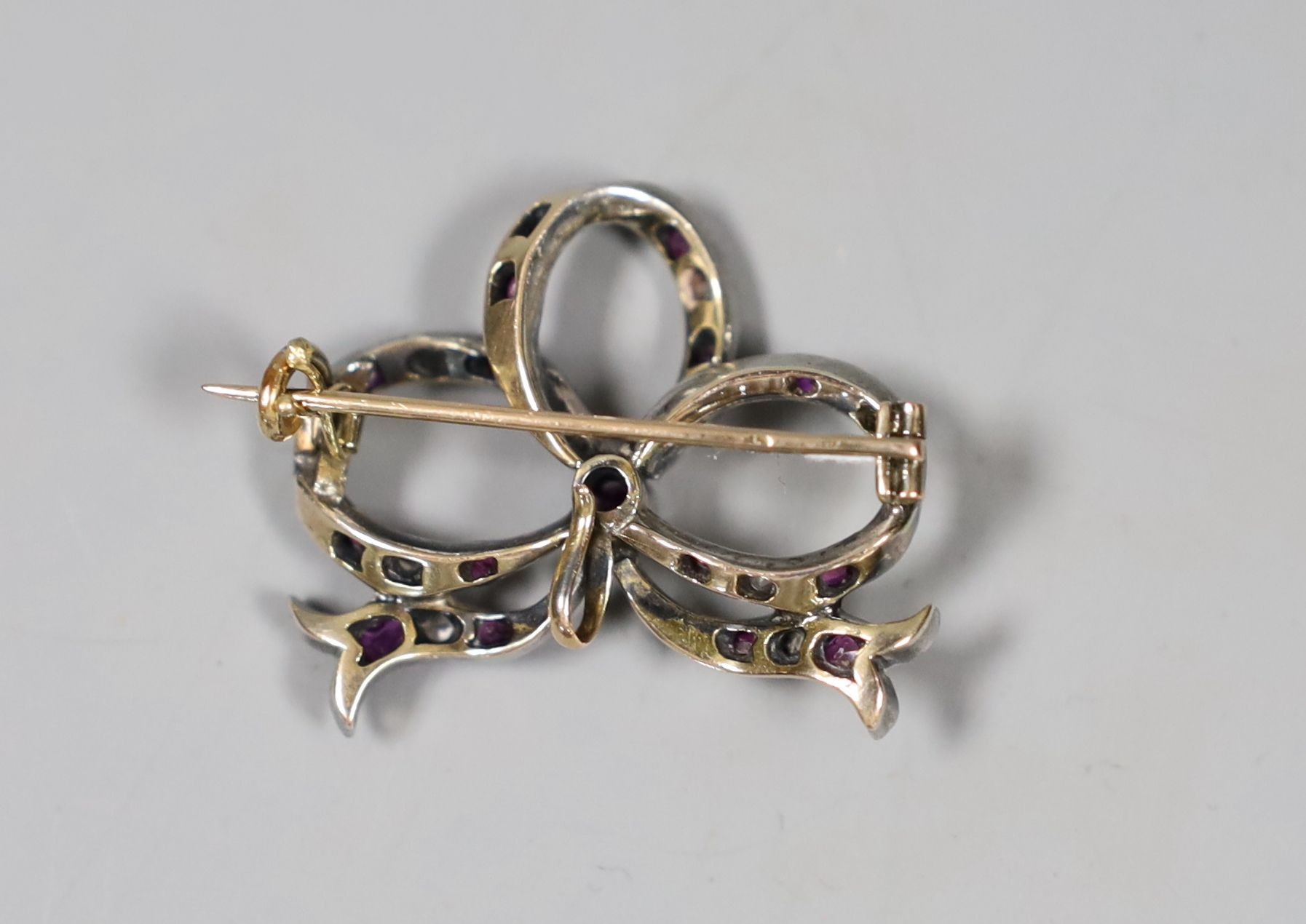 An early 20th century yellow metal, diamond and ruby set ribbon bow brooch, 31mm, gross 7.2 grams.